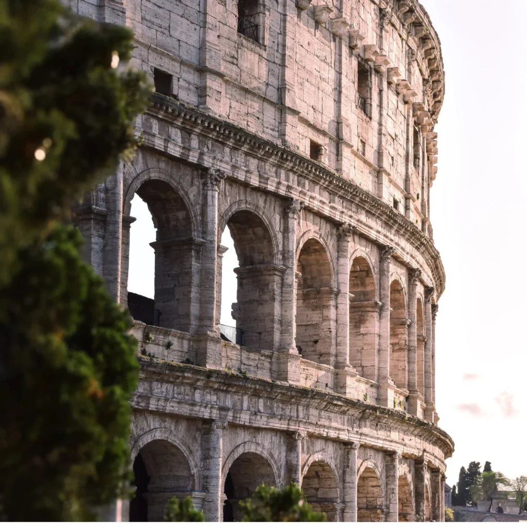 Close-up shot of the Colosseum's historic stone archways framed by green trees on a bright day in Rome, Italy